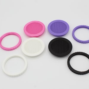 May include: Assortment of eight round plastic jar lids with different colors and designs. Some lids have a smooth surface, while others have a textured surface with small holes. The lids are in various colors, including pink, purple, white, and black.