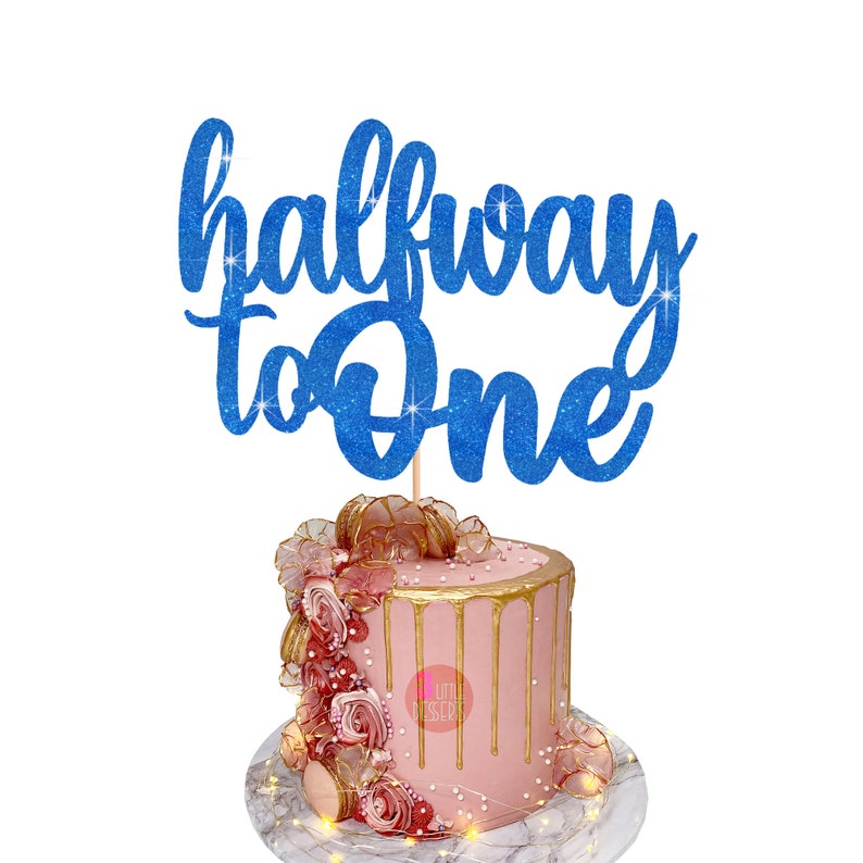 Puede incluir: Topper de pastel de purpurina azul con el texto "halfway to one". El topper est&aacute; encima de un pastel rosa con glaseado dorado de goteo y decoraciones de flores rosas y doradas.