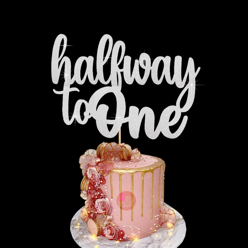 Puede incluir: Topper de pastel de purpurina plateada con el texto "halfway to one". El topper est&aacute; encima de un pastel rosa con glaseado dorado de goteo y decoraciones rosas y doradas.