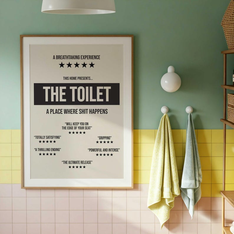 May include: A rectangular wall poster with a beige background and black text. The poster features a movie-style review layout with the title THE TOILET, five-star ratings, and phrases including A BREATHTAKING EXPERIENCE and A PLACE WHERE SHIT HAPPENS.
