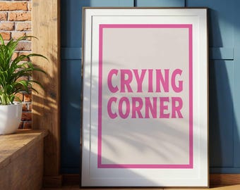 May include: A framed wall art print featuring a light beige background enclosed by a bold pink rectangular border. The text "CRYING CORNER" is printed in large, centered, pink capital letters within the border of the rectangular frame.