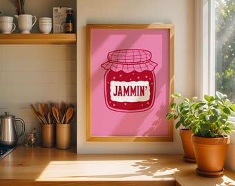 May include: A framed wall art print featuring a pink background with a central illustration of a red jar of jam. The jar has a checkered lid and a white label in the center with the word JAMMIN' printed in bold red capital letters.