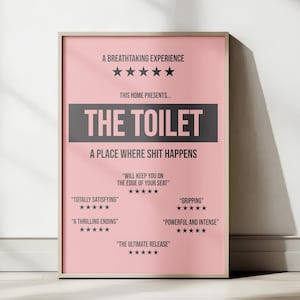 May include: A rectangular wall poster with a light pink background and dark gray text. The poster features the title THE TOILET in a large dark gray box, surrounded by five-star reviews and phrases like A BREATHTAKING EXPERIENCE and A PLACE WHERE SHIT HAPPENS, all framed in a thin light-colored wooden border.
