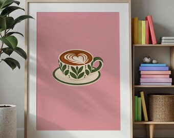 May include: A framed wall art print featuring a coffee cup on a saucer against a solid pink background. The cup and saucer are cream-colored with a green leaf pattern. The coffee has a heart-shaped foam design on the surface.