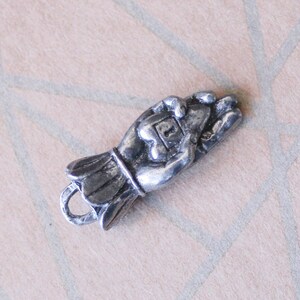 May include: Silver charm in the shape of a hand holding a small heart. The charm has a loop at the bottom for attaching to a bracelet or necklace.