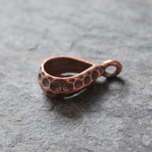 Op de afbeelding: Een koperkleurige hangerbeugel met een gehamerde textuur en een traanvorm.