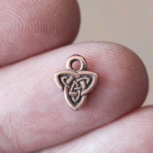 Könnte beinhalten: Ein kleiner, kupferfarbener Anhänger in Form eines keltischen Knotens. Der Knoten ist ein traditionelles Symbol für Liebe, Freundschaft und Ewigkeit.