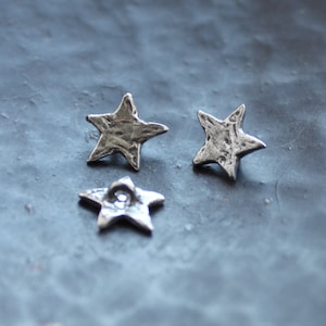 Könnte beinhalten: Drei silberne sternförmige Knöpfe mit einer strukturierten Oberfläche.
