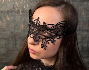 May include: Black lace eye mask with an intricate floral design. The mask covers the eyes and part of the forehead, secured with a thin strap. The mask is worn by a person.