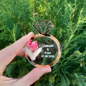 May include: A gold mirror ring with a diamond design and a small bouquet of dried flowers inside. The ring has the text "Giancarlo & Erica 07.06.2026" engraved on it.