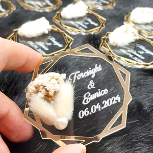 May include: A clear acrylic octagon-shaped wedding favor with a gold border. The favor features a dried flower arrangement and a pearl. The text "Foresight & Eunice 06.04.2024" is engraved on the acrylic.