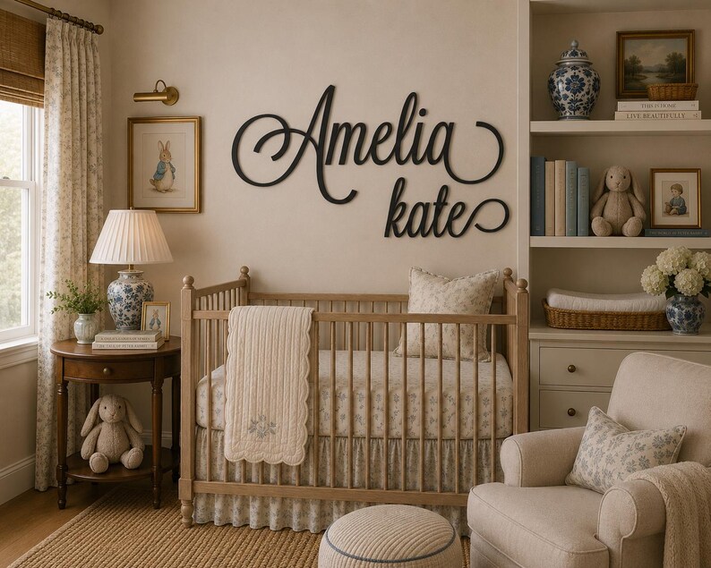 May include: A black script wall sign featuring the name Amelia Kate mounted above a wooden crib. The crib is dressed with a patterned sheet and a cream-colored quilted blanket. The room includes a side table, a lamp, and a bookshelf.