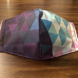 May include: A face mask with a geometric pattern in shades of purple, blue, and white. The mask has white elastic ear loops.