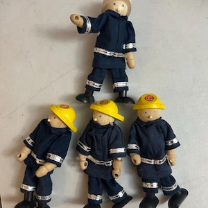 May include: Four wooden firefighter dolls with light skin tones and blue eyes. Each doll wears a dark blue uniform with silver reflective trim and black boots. Three dolls wear yellow helmets with a red F emblem, while one wears a tan helmet.