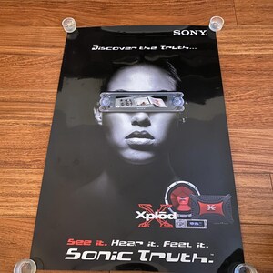 May include: A black poster with the Sony logo and the text "Discover the Truth...". The poster features a woman's face with a car stereo graphic over her eyes and "Xplod" branding. The text "See it. Hear it. Feel it. Sonic Truth." is also visible.