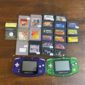 Puede incluir: Una colección de cartuchos de Game Boy Advance y dos consolas Game Boy Advance. Los cartuchos presentan varios títulos de juegos. Una consola es morada, la otra es verde. El texto "GAME BOY ADVANCE" es visible en las consolas.