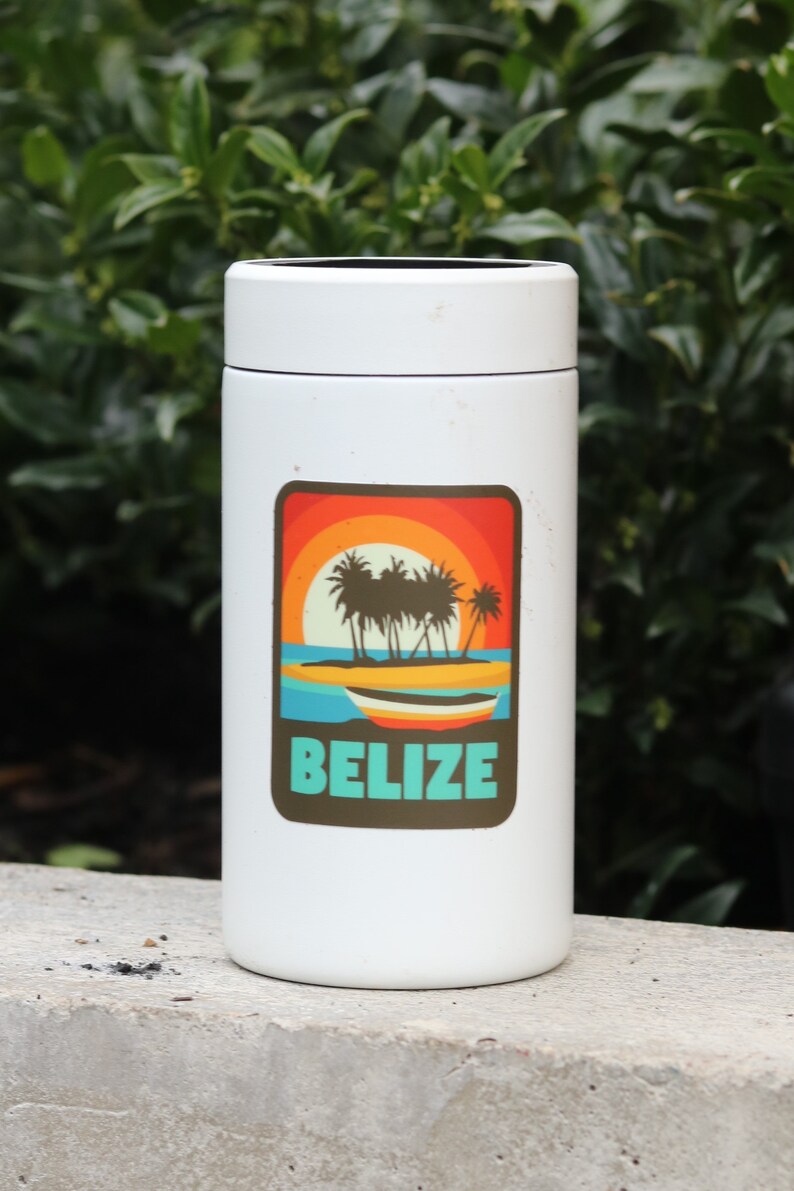May include: White travel mug with a sticker featuring a sunset scene with palm trees and a boat. The sticker says "Belize" in turquoise text.