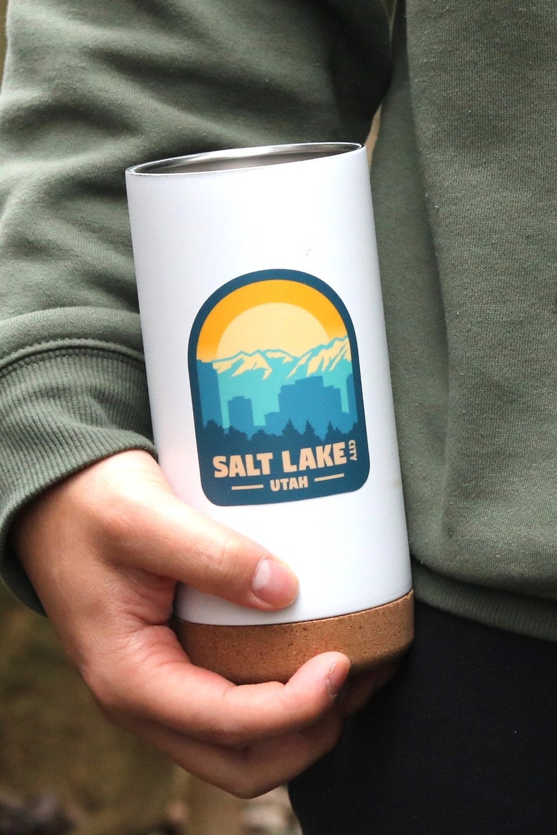 May include: White travel mug with a cork bottom and a sticker featuring a mountain range and the text "SALT LAKE CITY UTAH".