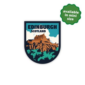 May include: A shield-shaped sticker featuring a graphic illustration of Edinburgh Castle in Scotland, set against a light blue sky with white clouds, brown rocky terrain, and green foliage, with the text EDINBURGH SCOTLAND at the top.