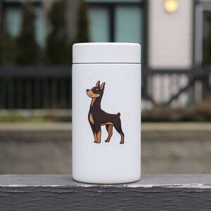 May include: White insulated travel mug with a brown and black dog sticker on the front. The dog is looking to the left.