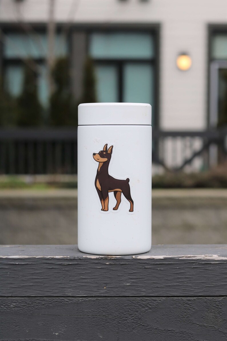 May include: White insulated travel mug with a brown and black dog sticker on the front. The dog is looking to the left.