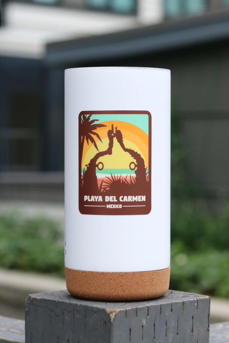 Pode incluir: Caneca de viagem branca com fundo de corti&ccedil;a. A caneca tem um adesivo com uma cena de p&ocirc;r do sol e o texto "Playa del Carmen - M&eacute;xico".