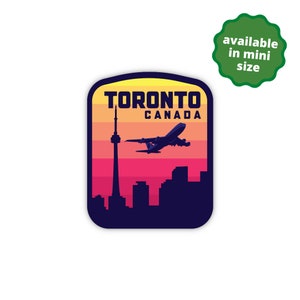 May include: A retro-style sticker featuring a silhouette of the Toronto skyline with the CN Tower and an airplane flying over it. The sticker has a yellow, orange, and red sunset background with the text "TORONTO CANADA" in white.