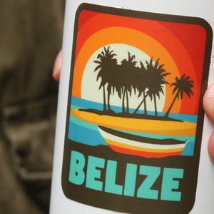 May include: A white travel mug with a sticker featuring a sunset scene with palm trees and a boat. The sticker says "Belize" in turquoise text.