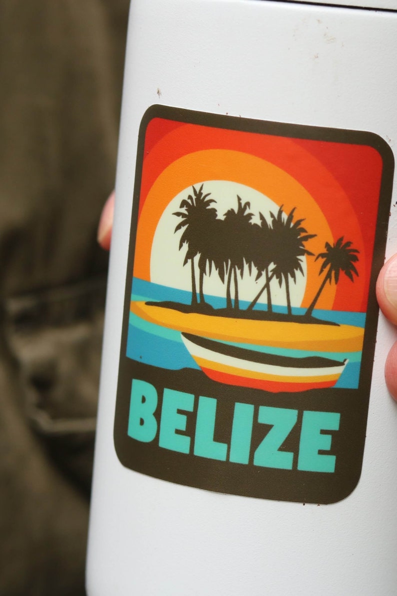 May include: A white travel mug with a sticker featuring a sunset scene with palm trees and a boat. The sticker says "Belize" in turquoise text.