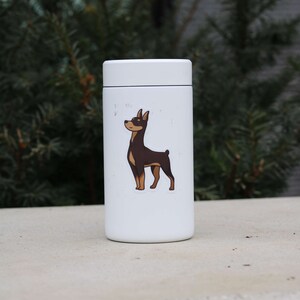 May include: White insulated water bottle with a brown and black dog sticker. The dog is looking up and has its tongue out.