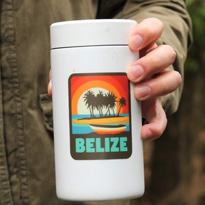 May include: White travel mug with a sticker featuring a sunset scene with palm trees and a boat. The sticker says "BELIZE" in turquoise text.