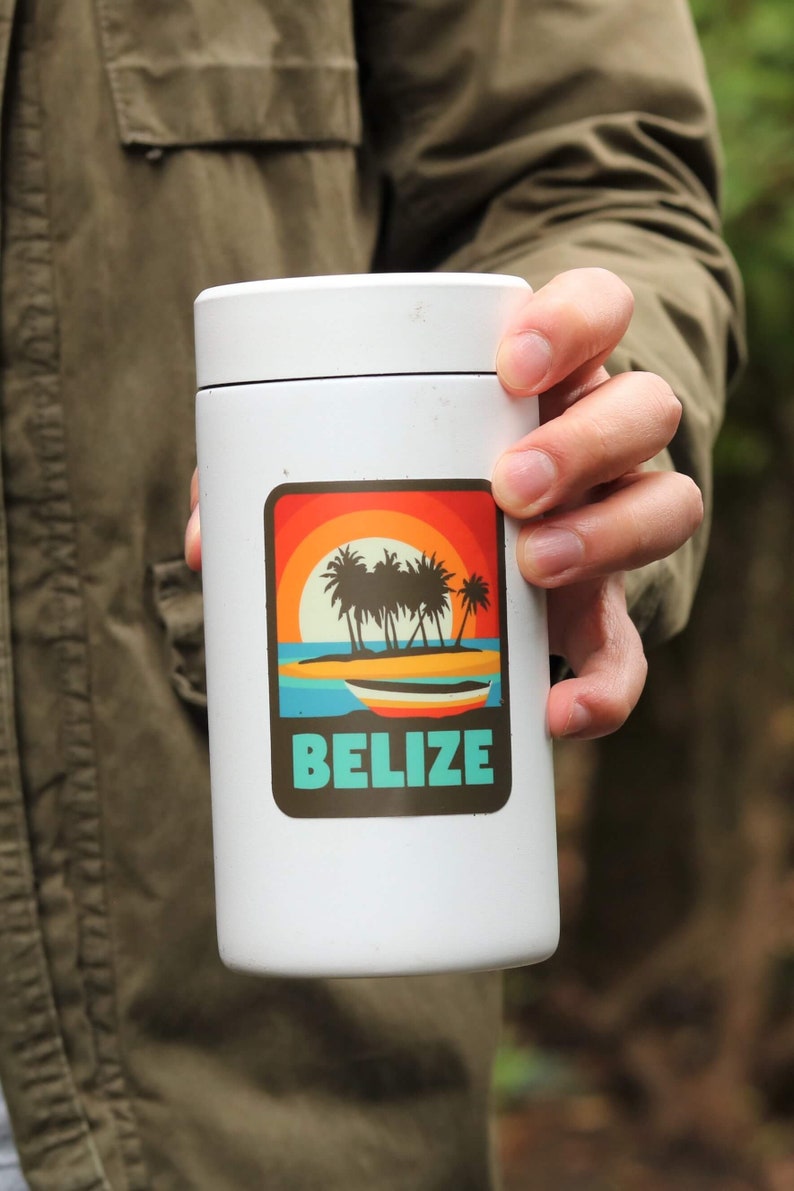 May include: White travel mug with a sticker featuring a sunset scene with palm trees and a boat. The sticker says "BELIZE" in turquoise text.