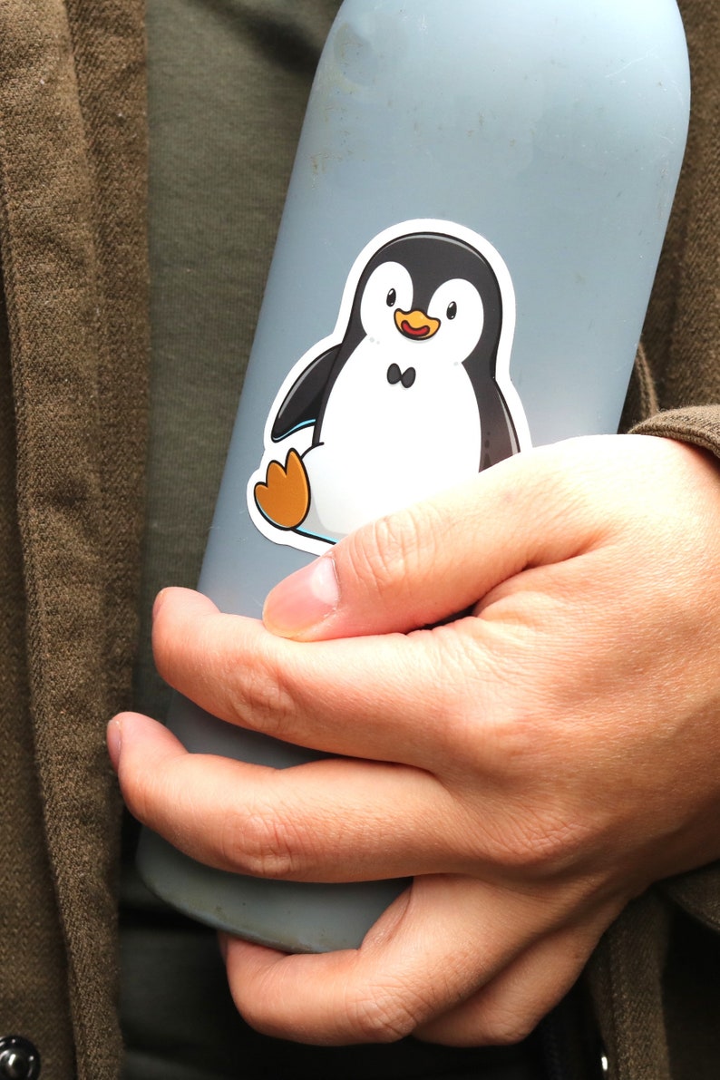 Puede incluir: Una botella de agua azul claro con una pegatina de ping&uuml;ino. El ping&uuml;ino es negro y blanco con patas naranjas. La botella la sostiene una persona que lleva una camisa verde y una chaqueta marr&oacute;n.