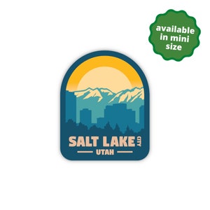 May include: A blue and yellow sticker with a silhouette of the Salt Lake City skyline, mountains, and a sun. The text "SALT LAKE CITY - UTAH" is printed below the skyline.
