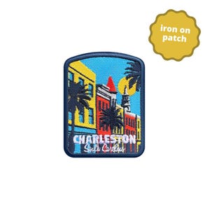 May include: A rectangular iron-on patch featuring an embroidered scene of Charleston, South Carolina. The design displays colourful buildings in yellow, red, and blue, palm trees, a steeple, and a yellow sun against a blue sky. The text reads Charleston South Carolina.