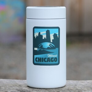 May include: White insulated tumbler with a blue and white sticker featuring a skyline of Chicago, Illinois. The sticker says "Illinois Chicago".