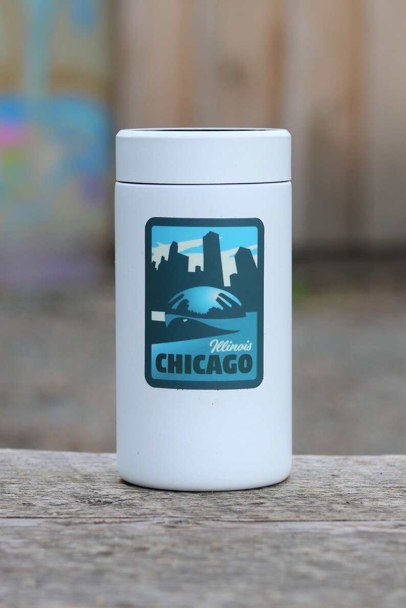 May include: White insulated tumbler with a blue and white sticker featuring a skyline of Chicago, Illinois. The sticker says "Illinois Chicago".