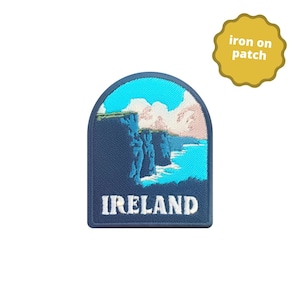 May include: An iron-on patch featuring an embroidered image of a cliffside overlooking a body of water, in blue and white. The text "IRELAND" is embroidered in white on a dark blue background.