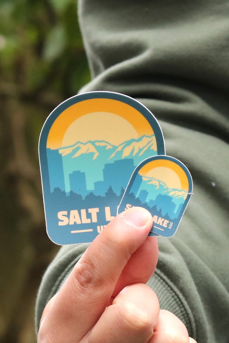 May include: Two stickers with a blue, yellow, and white mountain range design. The larger sticker says "SALT LAKE CITY, UT" and the smaller sticker says "SALT LAKE CITY".