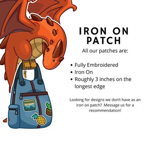 K&ouml;nnte beinhalten: Ein orangefarbener Zeichentrickdrache h&auml;lt eine blaue Jeans-Tasche mit Aufn&auml;hern. Die Tasche hat einen Denver-Aufn&auml;her, einen Kaktus und eine Ananas. Der Text lautet "IRON ON PATCH" und "Etwa 7,6 cm an der l&auml;ngsten Kante."