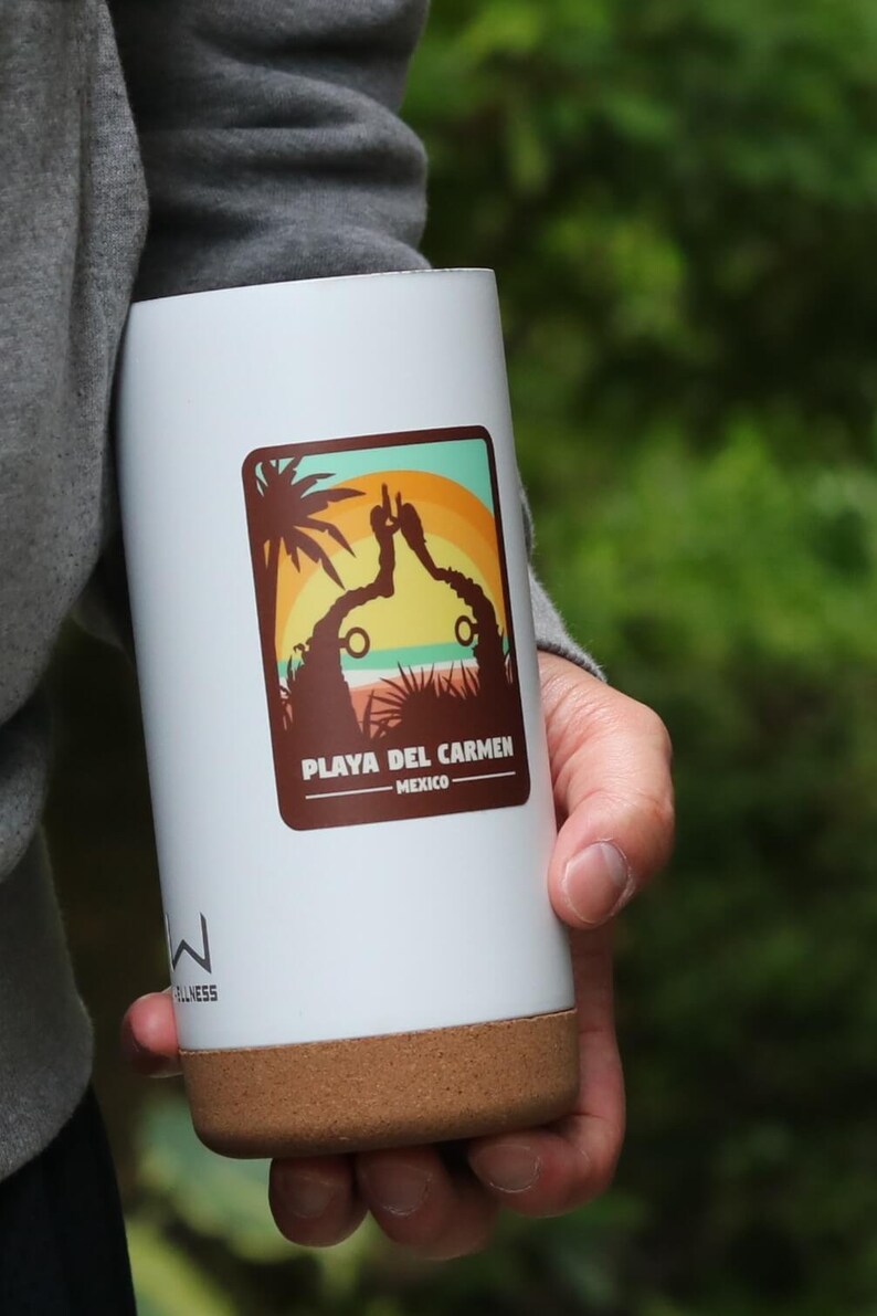 Pode incluir: Caneca de viagem branca com fundo de corti&ccedil;a marrom. A caneca tem um adesivo com uma cena de p&ocirc;r do sol e o texto "Playa del Carmen - M&eacute;xico".