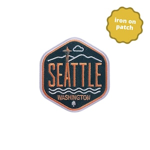 May include: An iron-on patch with a dark teal background and an orange and white design. The patch features the word "SEATTLE" in orange, the Space Needle, and the word "WASHINGTON". The patch is in a hexagon shape.