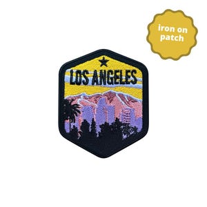 May include: Iron-on patch featuring a yellow sunset over a purple cityscape with palm trees and the text "LOS ANGELES" in black.