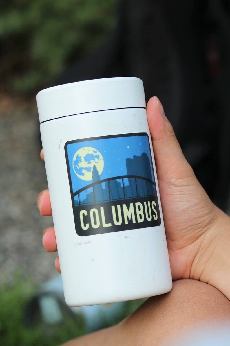 May include: White insulated travel mug with a sticker featuring a skyline and the word "COLUMBUS" in yellow letters.