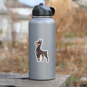 May include: A silver water bottle with a black lid and a sticker of a brown and tan dog on the side.