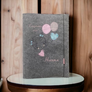 Könnte beinhalten: Grauer Filz-Fotoalbum mit gestickter Mädchenfigur, die Ballons hält, und dem Text "Zaugnisse von Hanna".
