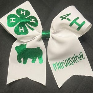 May include: White bow with green glitter 4-H clover and a green glitter silhouette of a pig. The bow also has the text "4-H" and "marialsabel" in green glitter.
