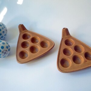 Può includere: Due piatti triangolari marroni per lumache con sette rientranze circolari ciascuno e un piccolo manico. Sono visibili anche tre palline decorative blu e bianche con motivi floreali e a pois.