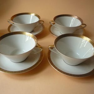 Puede incluir: Juego de cuatro cuencos de sopa de porcelana blanca con platillos a juego. Cada cuenco y platillo presenta un borde dorado y una banda dorada. Los cuencos tienen asas pequeñas.