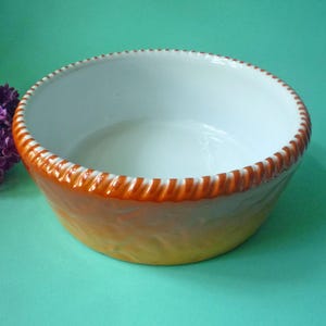 Op de afbeelding: Een witte keramische kom met een bruine en oranje rand. De kom heeft een getextureerd ontwerp aan de buitenkant.